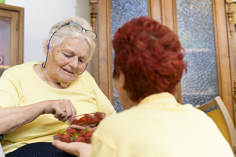 Eine Seniorin prüft eine Erdbeere.