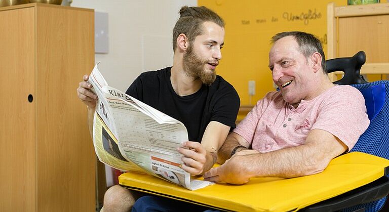 Heilerziehungspfleger liest mit einem Mann mit Behinderung die Zeitung in der Förderstätte Himmelkron