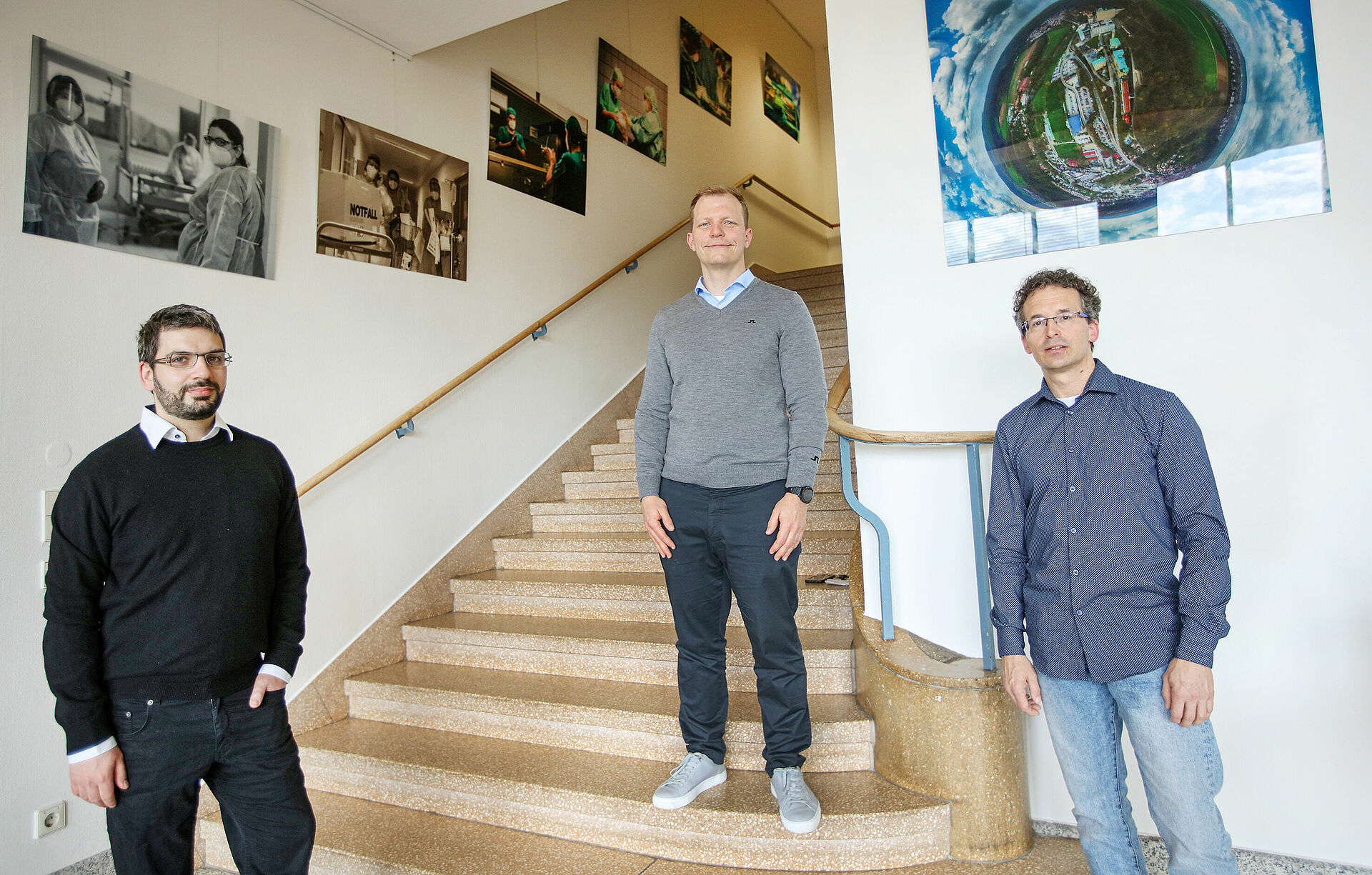 Drei Männer stehen in einem mit Bildern geschmückten Treppenhaus