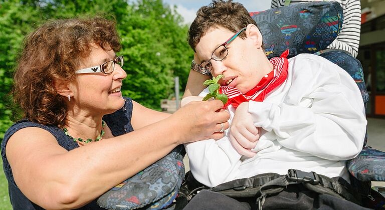Mitarbeiterin der Förderstätte Neuendettelsau bietet einer Frau mit Behinderung Minze zum riechen an