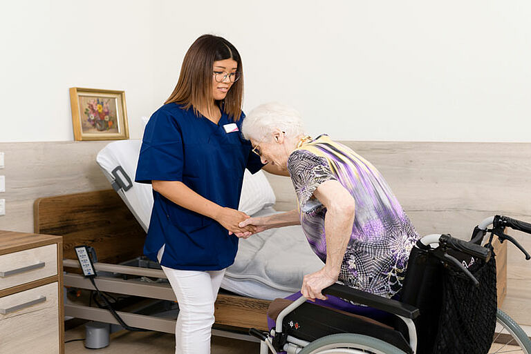 Pflegerin unterstützt eine Seniorin bei der Mobilisierung.