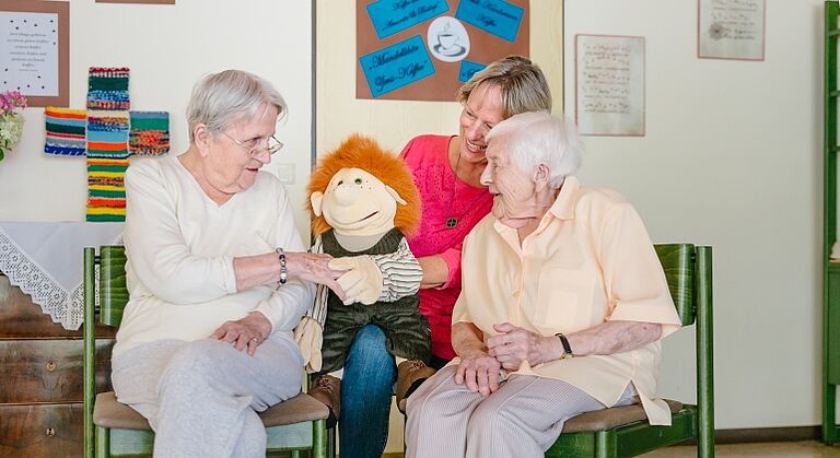 Gesprächsförderung von Menschen mit Demenz mit Handpuppe - gerontopsychiatrische Fachkraft mit zwei Bewohnerinnen im Therese Stählin Heim in Neuendettelsau im Kreis Ansbach