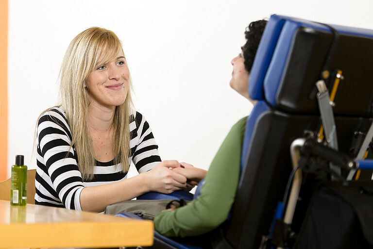Eine Schülerin der Fachschule für Heilerziehungspflege in Neuendettelsau im Kontakt mit einer Frau im Rollstuhl.