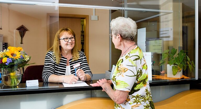 Freundliches Gespräch zwischen einer Bewohnerin und einer Mitarbeiterin an der Rezeption des Seniorenhofs Altdorf bei Nürnberg