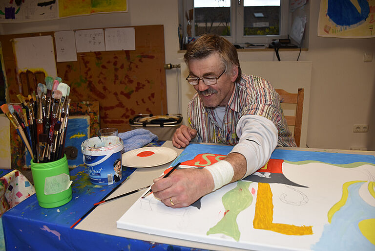 Mann mit Behinderung malt mit Wasserfarben.